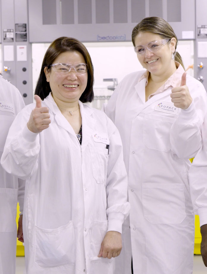 Image de deux femmes portant un sarrau blanc et des lunettes de sécurité avec le pouce levé.